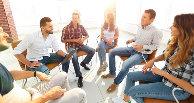 People sitting in chairs in circle discussing a topic. 