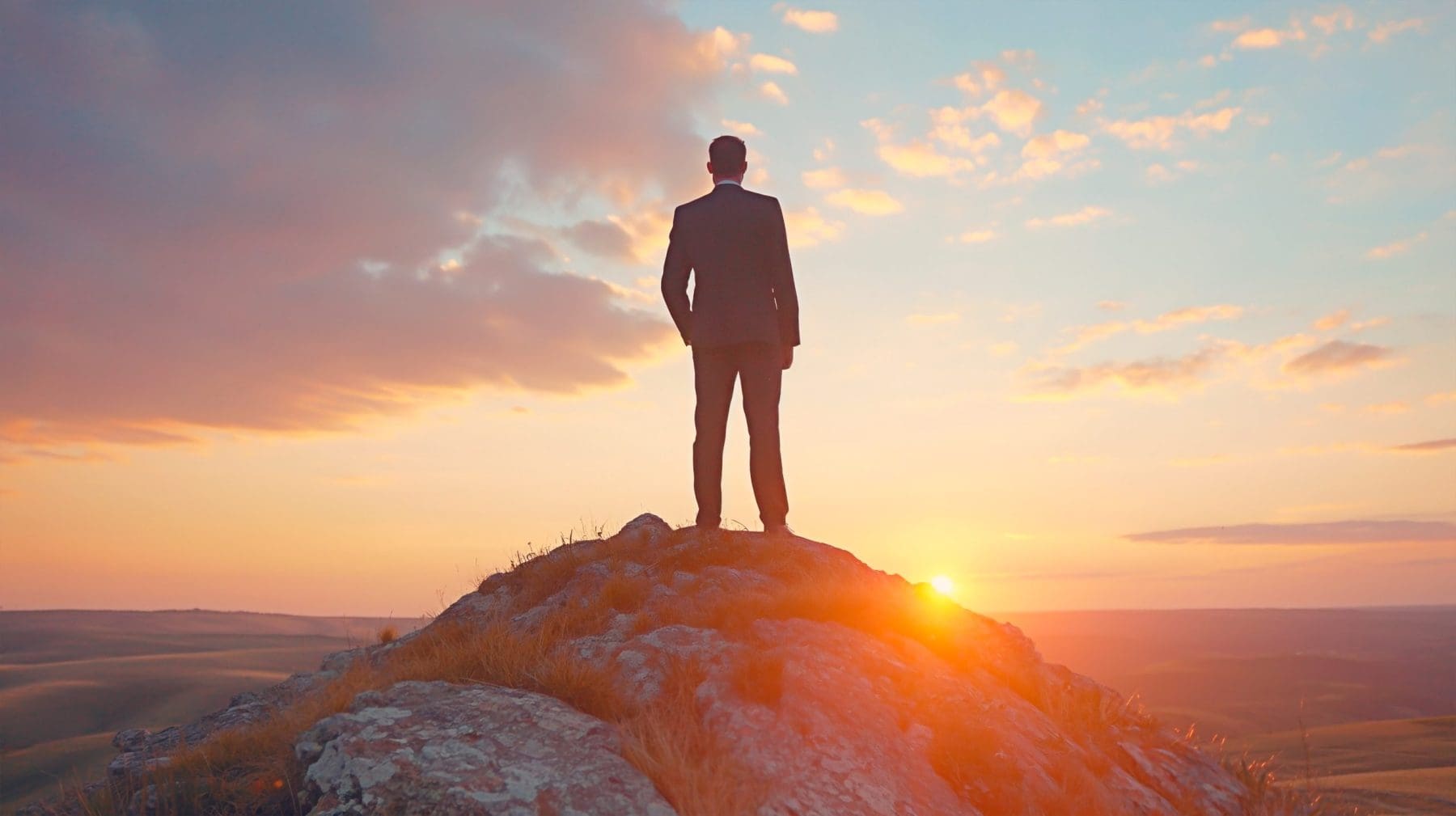 Concept of success and growth in business career. Business man on top of a hill during sunset.