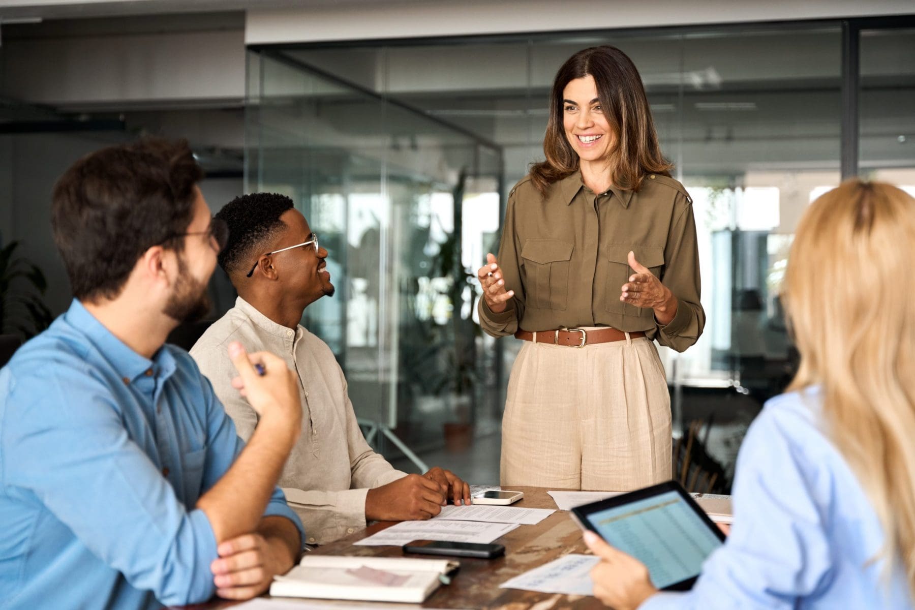 A woman addresses a group seated around a conference table. Her animated gestures and the team's engagement create a sense of open communication and enthusiasm.