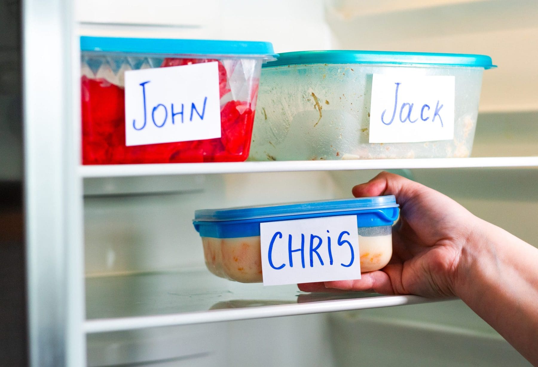Plastic food containers with name stickers in spacious office fridge.