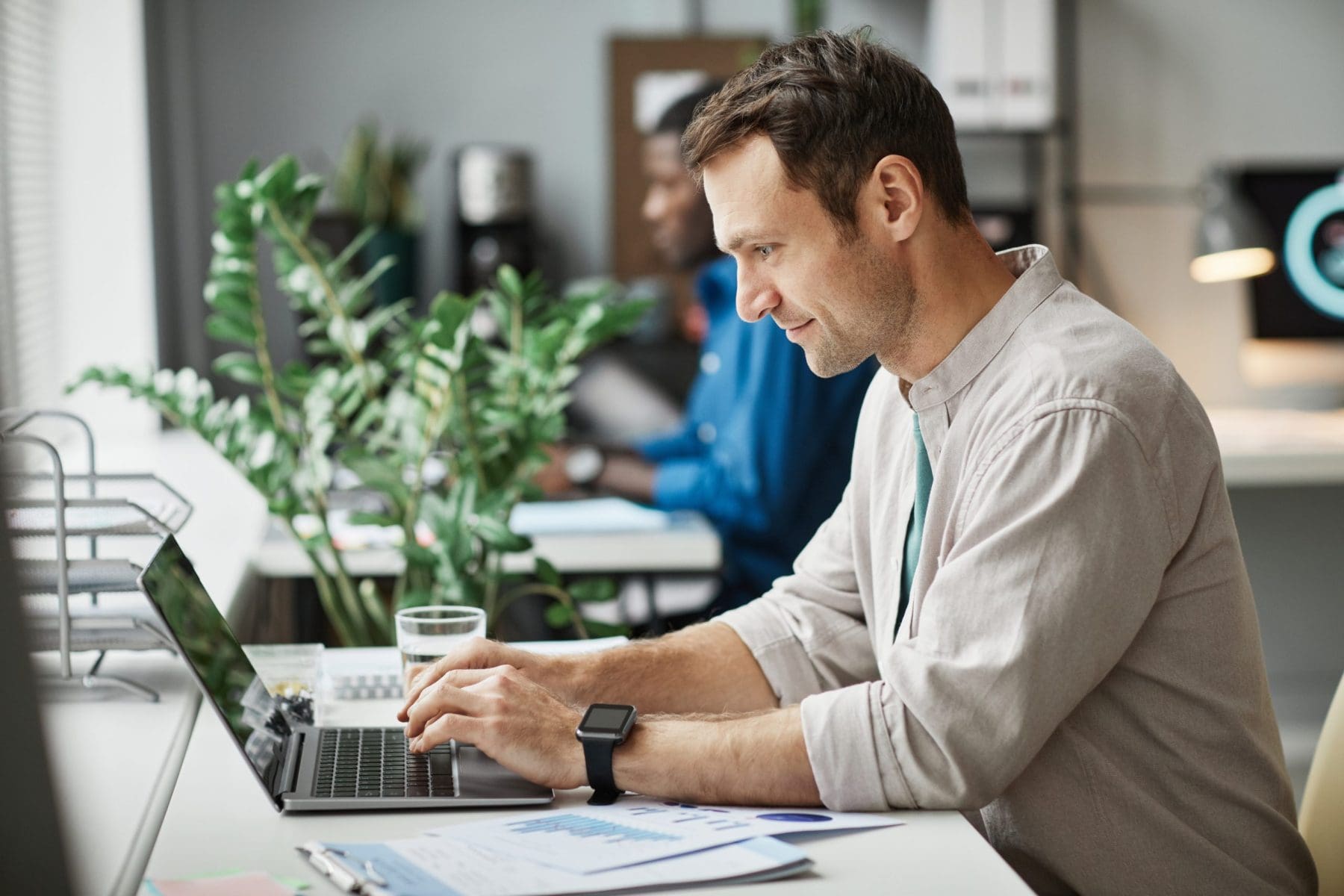 Side view portrait of smiling adult man using laptop while enjoying work in office.