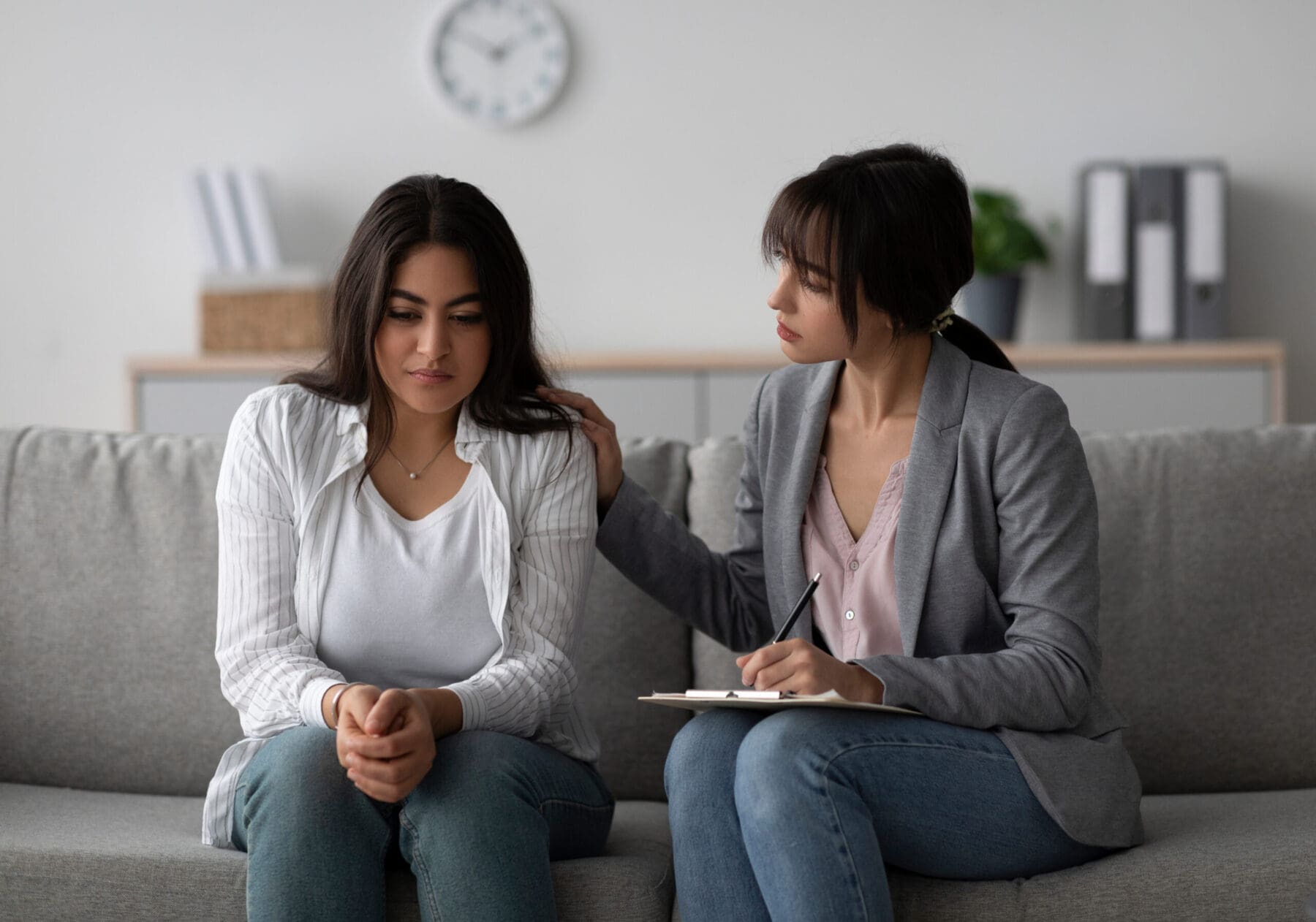 Woman comforts another woman while sitting on couch.