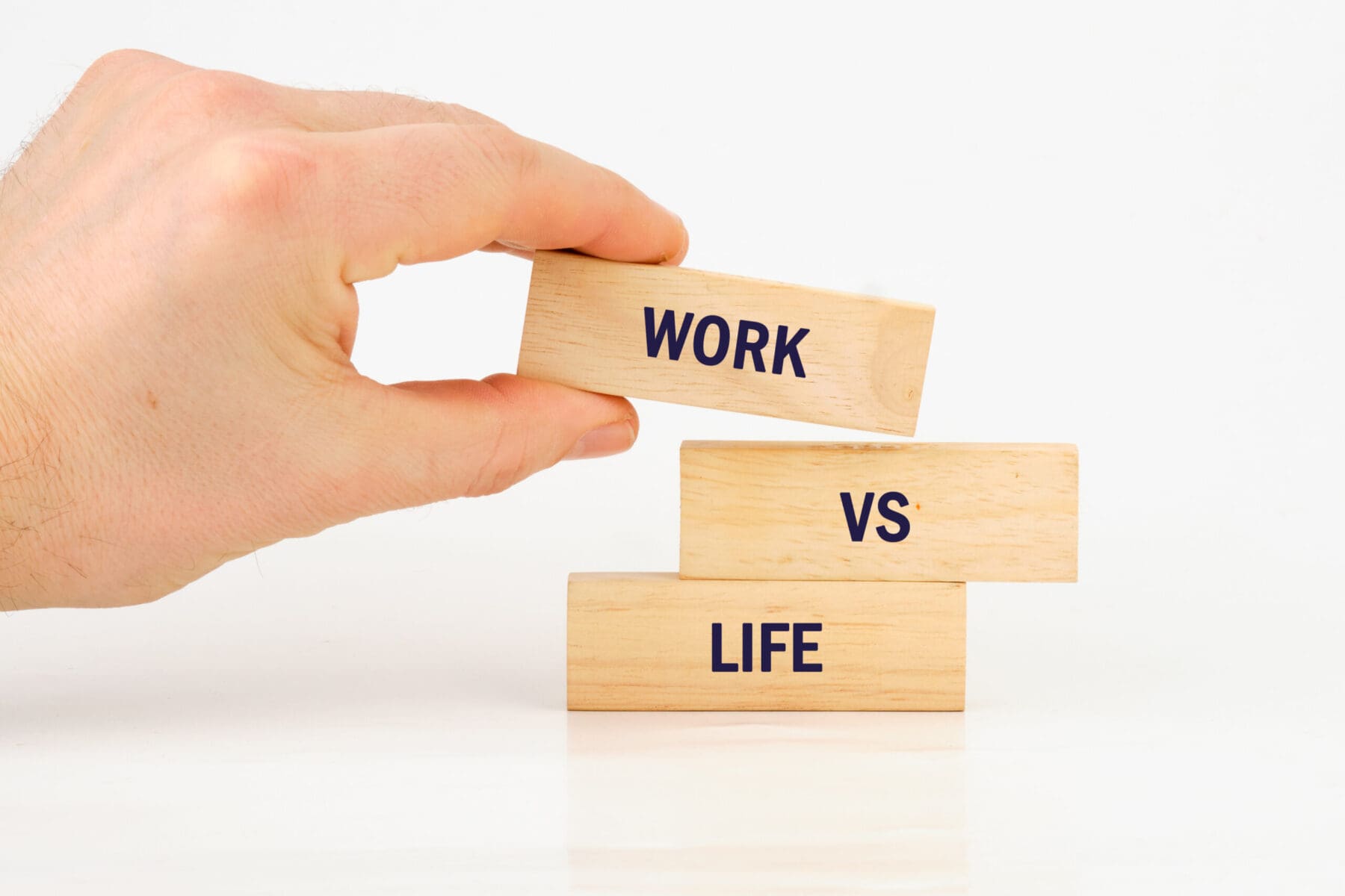 A hand carefully balances a wooden block labeled Work on top of blocks saying VS and Life.
