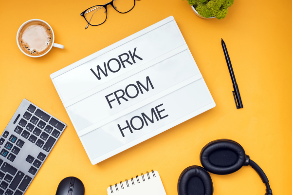 Words: Work from home. On desk with pen, glasses, and other items.