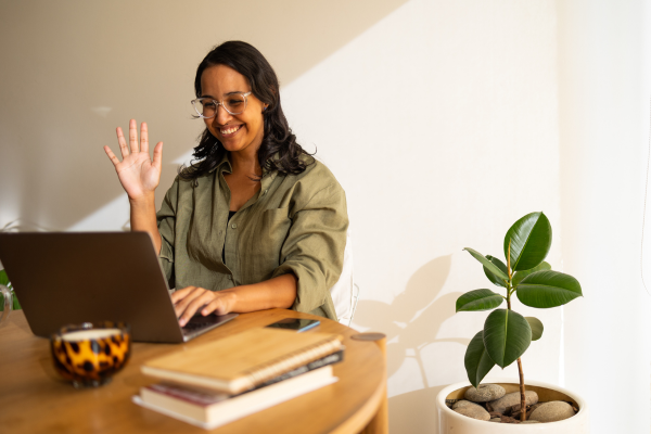 Woman waving at computer and smiling.