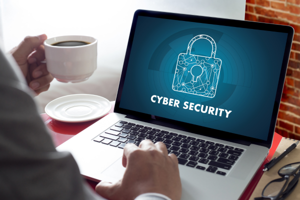 Person drinking coffee and working on laptop with lock on screen and words cybersecurity.