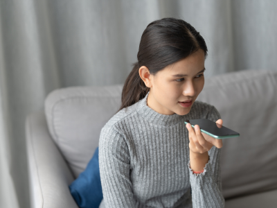 Woman speaking to her phone while sitting on couch.