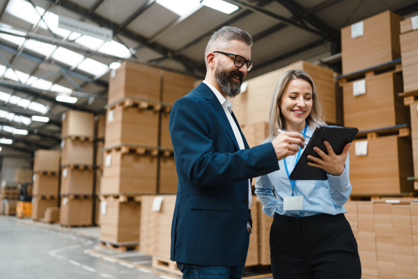 Man and woman looking at tablet, in warehouse space full of boxes.