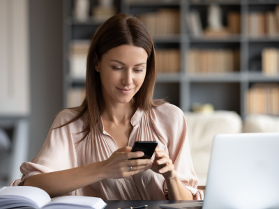 Woman looking at phone while working on laptop