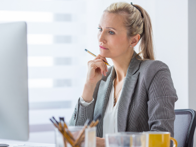 Woman looking at monitor while holding a pen on her chin.